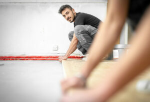 Junger Bodenleger-Lernender verlegt präzise einen Holzboden bei Schiess Wohntextil.