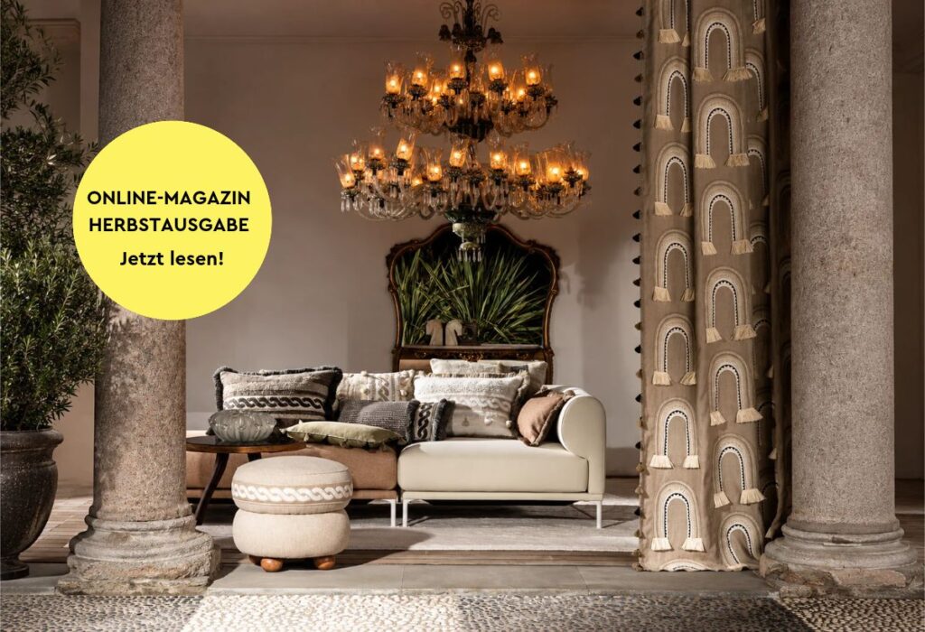 Elegantes Wohnzimmer mit cremefarbenem Sofa, strukturierten Kissen in Sand- und Grautönen, Polsterhocker und bodenlangem Vorhang mit gestickten Bogenmotiven